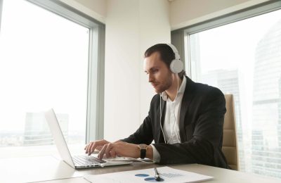 Businessman takes part in online meeting, conference, live stream, communicates with colleagues or partners via internet telephony. Guy listening music while working on laptop in office. Online study