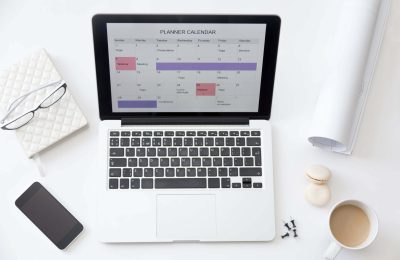 High angle view image of a working desk. Open laptop on the desk with a planner calendar on the screen. Business concept photo, close up